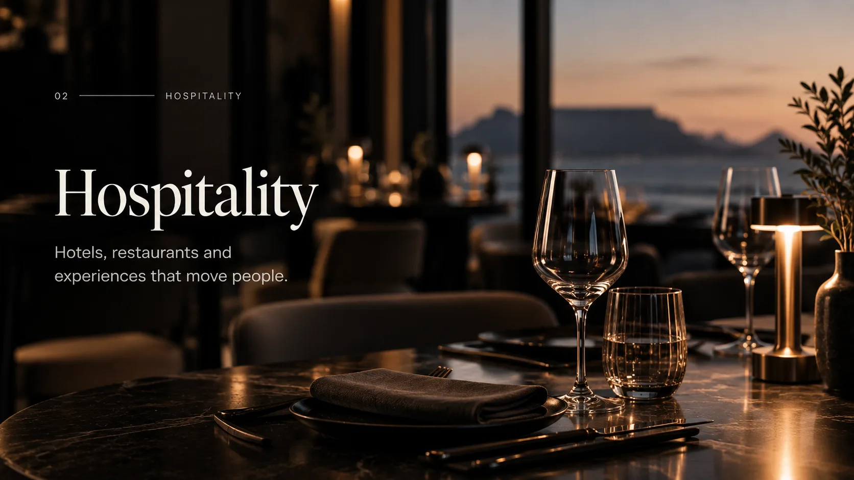 An intimate restaurant table set at dusk with a coastal view beyond